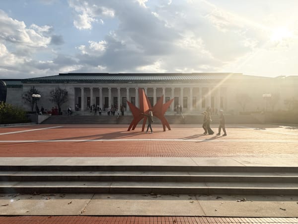 Front entrance of Toledo Museum with modern orange steel sculpture, sun flare from low afternoon light.